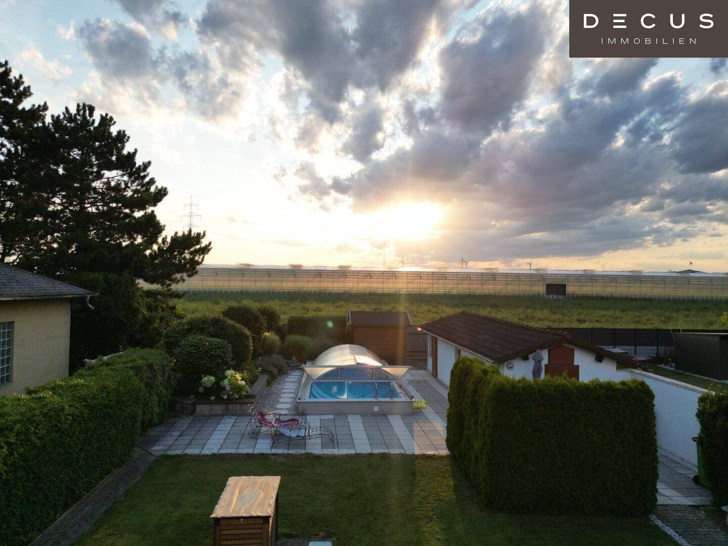 Gartenbereich mit Pool, Terrasse und gepflegter Grünfläche im warmen Licht des Sonnenuntergangs.