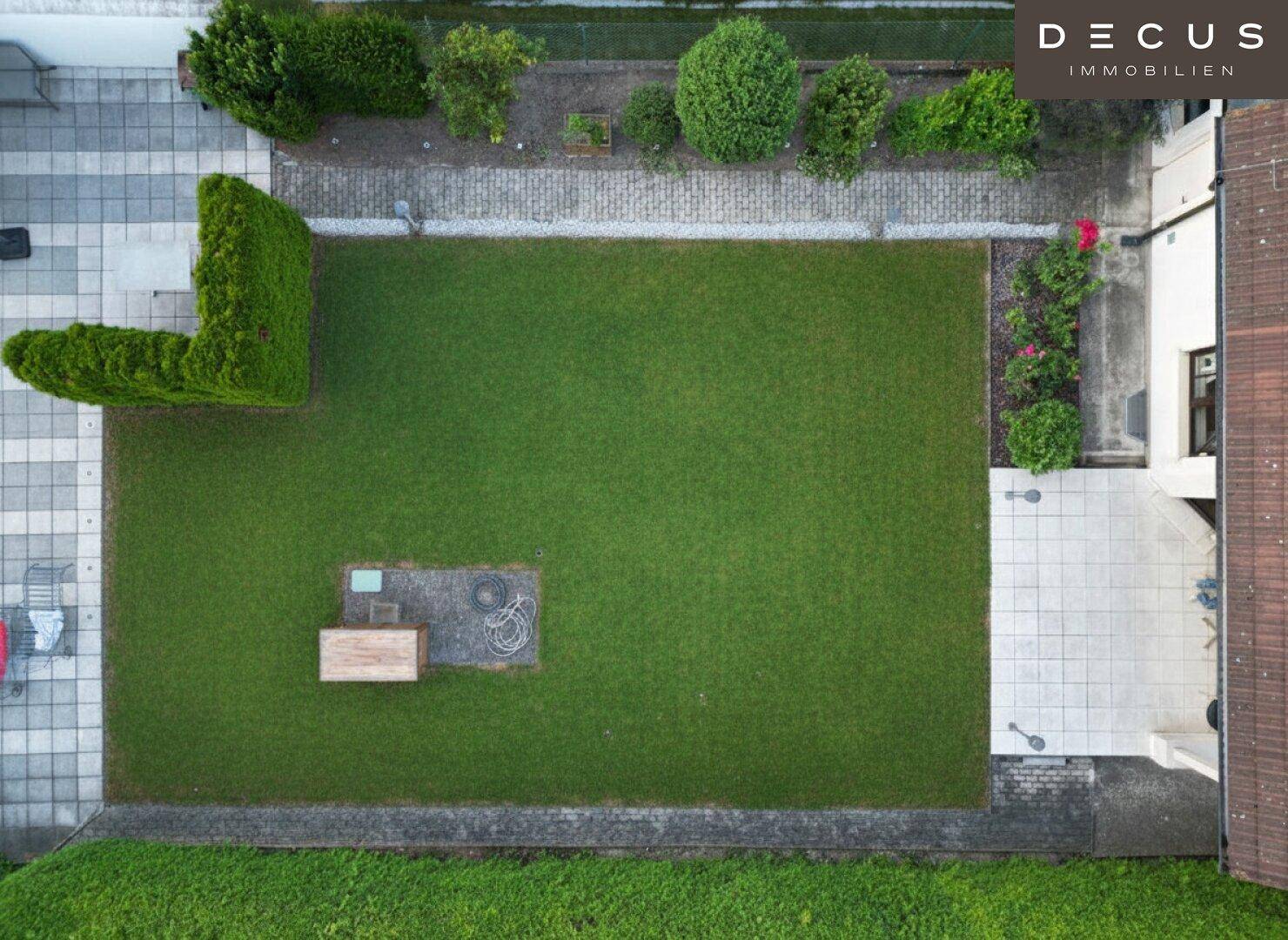 Vogelperspektive des gepflegten Gartens mit Rasenfläche, Terrasse und Hecken.