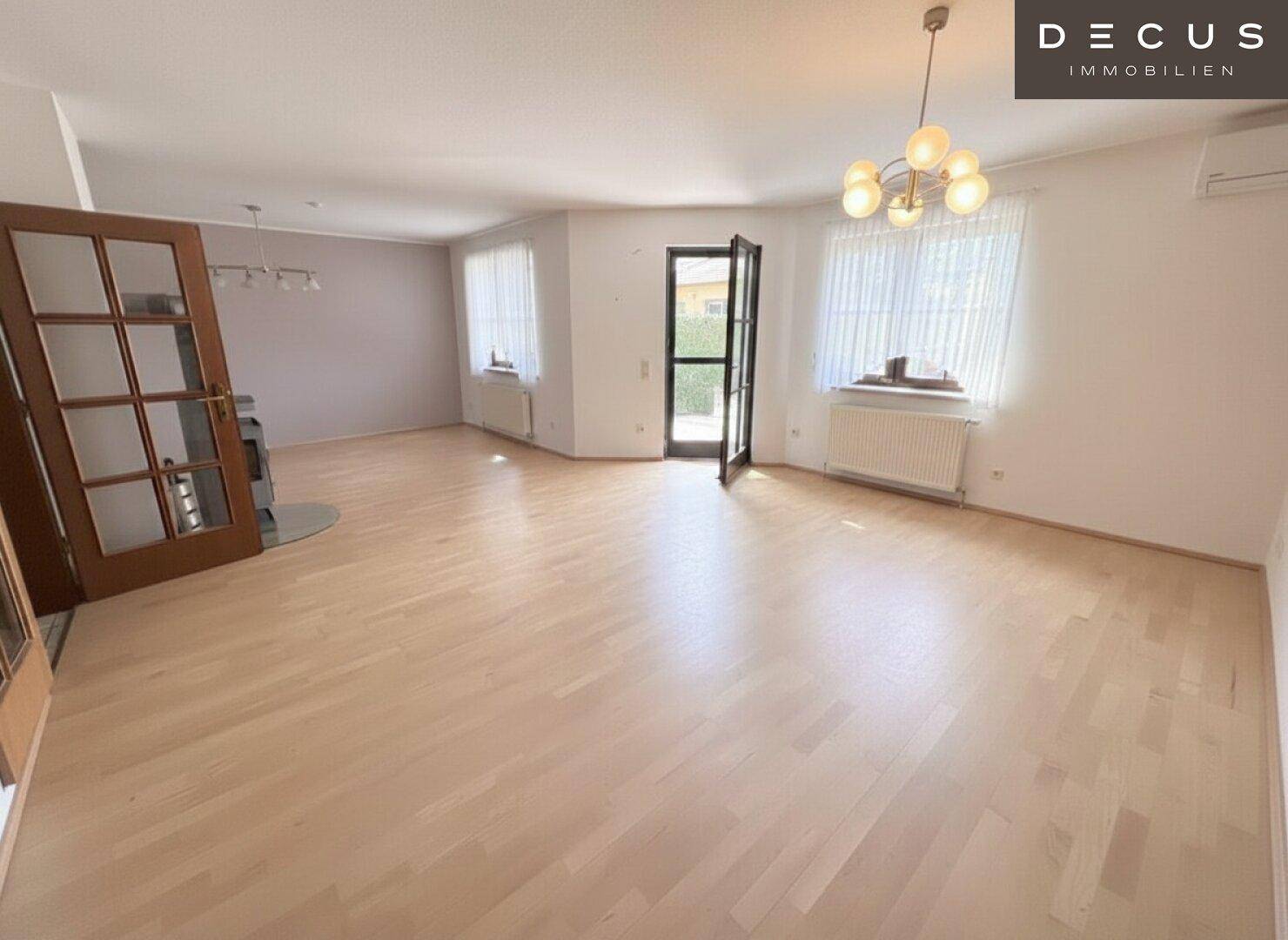 Helles Wohnzimmer mit Holzboden, Kaminofen und großen Fenstern für viel Tageslicht.