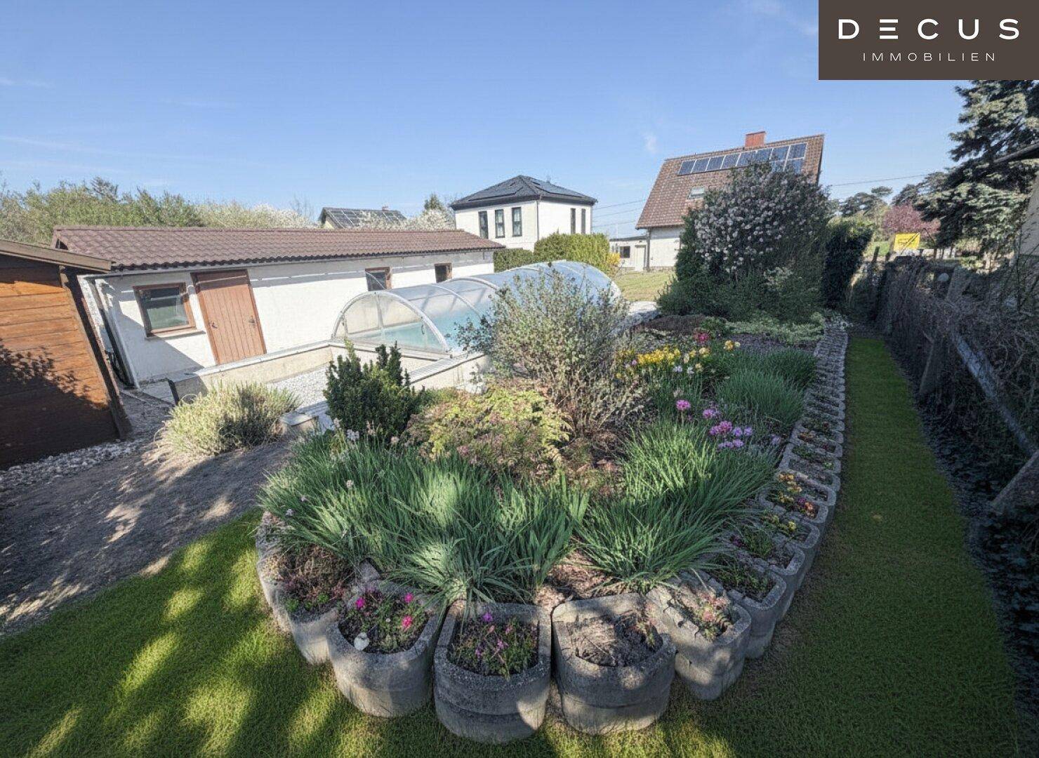 Bunter Gartenbereich mit verschiedenen Pflanzen und Blumen, im Hintergrund der Poolbereich.