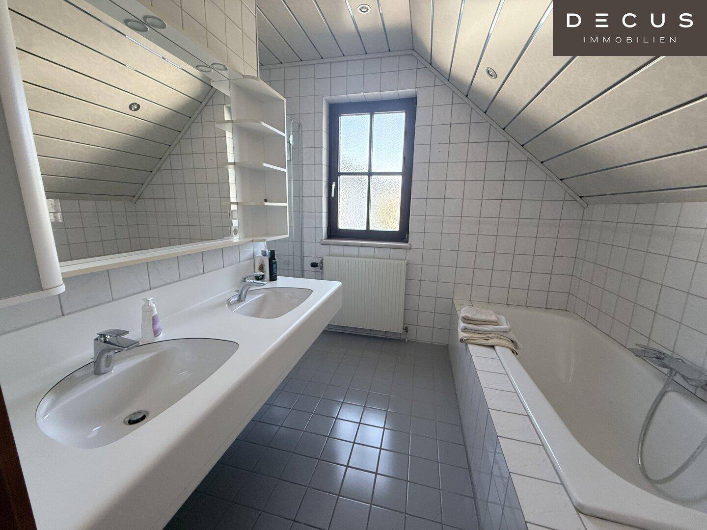 Geräumiges Badezimmer mit Doppelwaschbecken, Badewanne und Dachschräge.