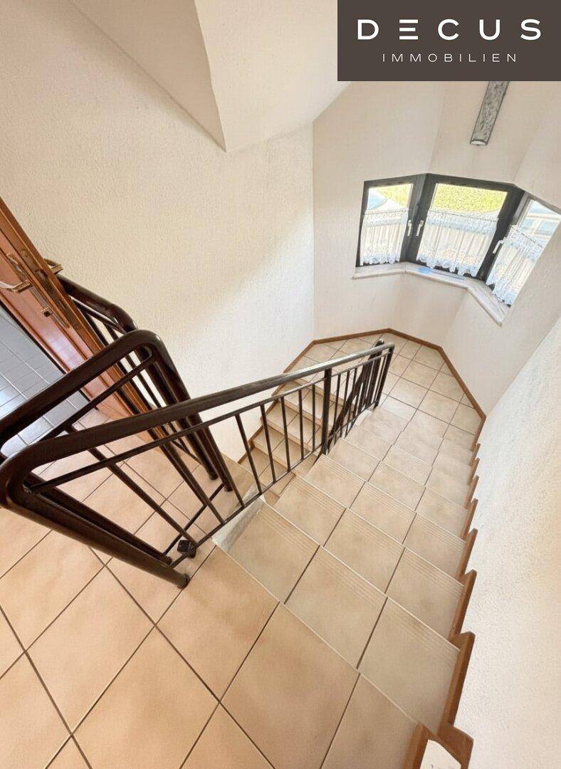 Geflieste Treppe mit Metallgeländer und einem Erkerfenster, das Tageslicht hereinlässt.