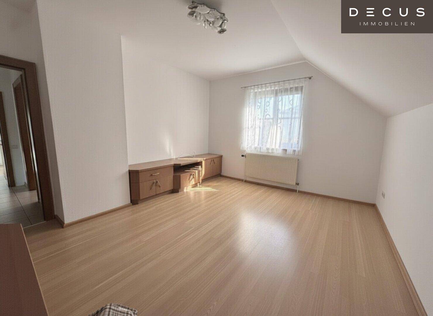Leeres Zimmer mit Laminatboden, Fenster und Dachschräge, bereit zur individuellen Gestaltung.