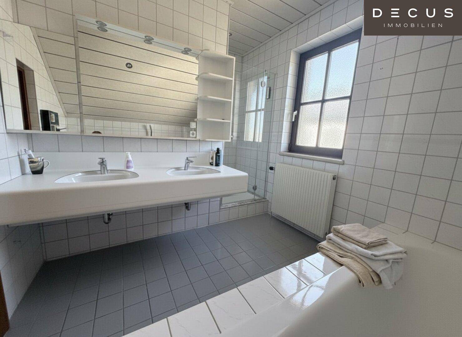 Helles Badezimmer mit Doppelwaschbecken, Badewanne und Duschbereich unter der Dachschräge.