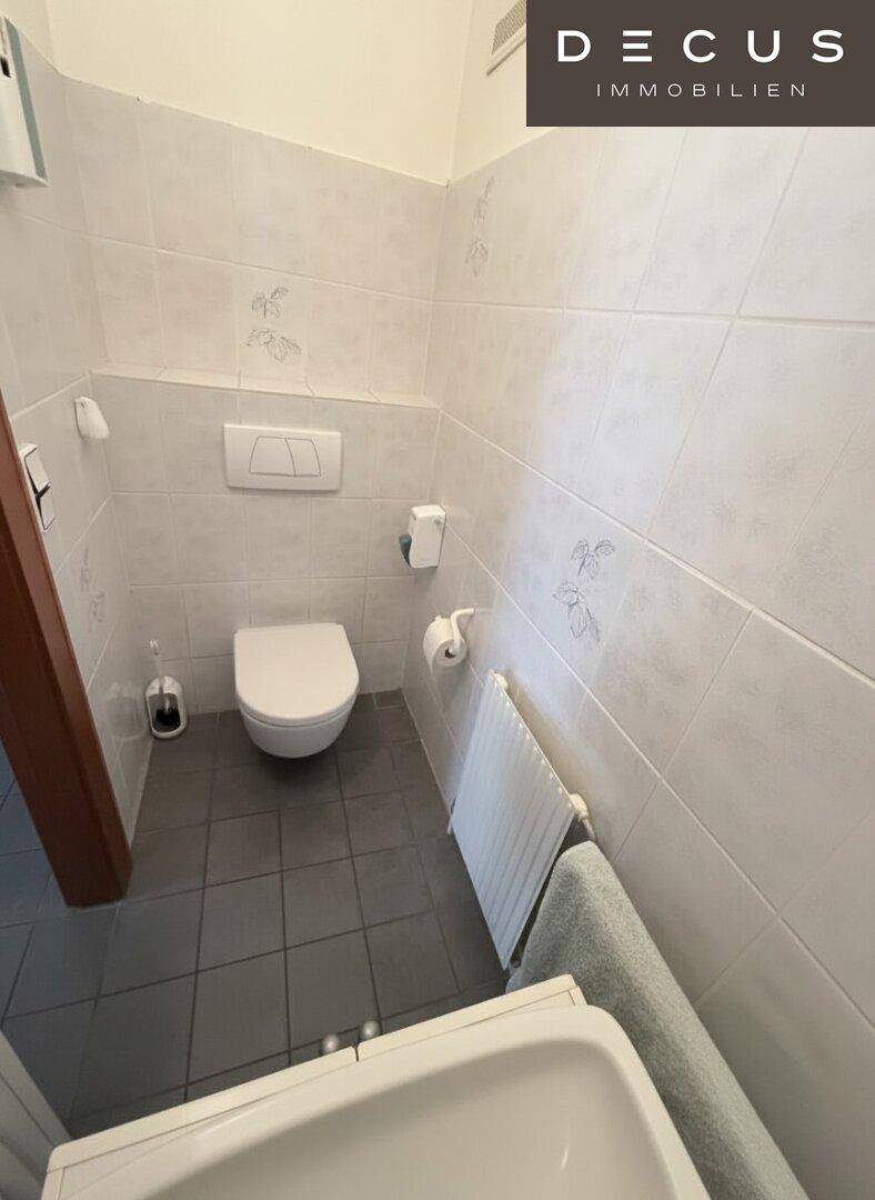Kleines Gäste-WC mit Wand-WC, Waschbecken und hellen Fliesen an Wänden und Boden.