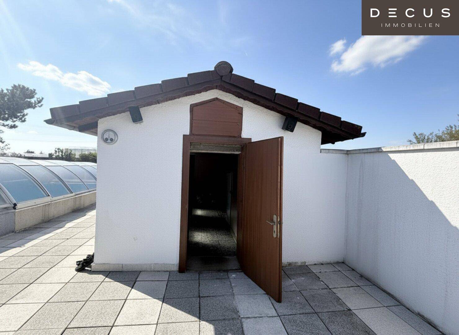 Kleines Nebengebäude mit offener Tür neben dem Poolbereich, umgeben von einer Terrasse.