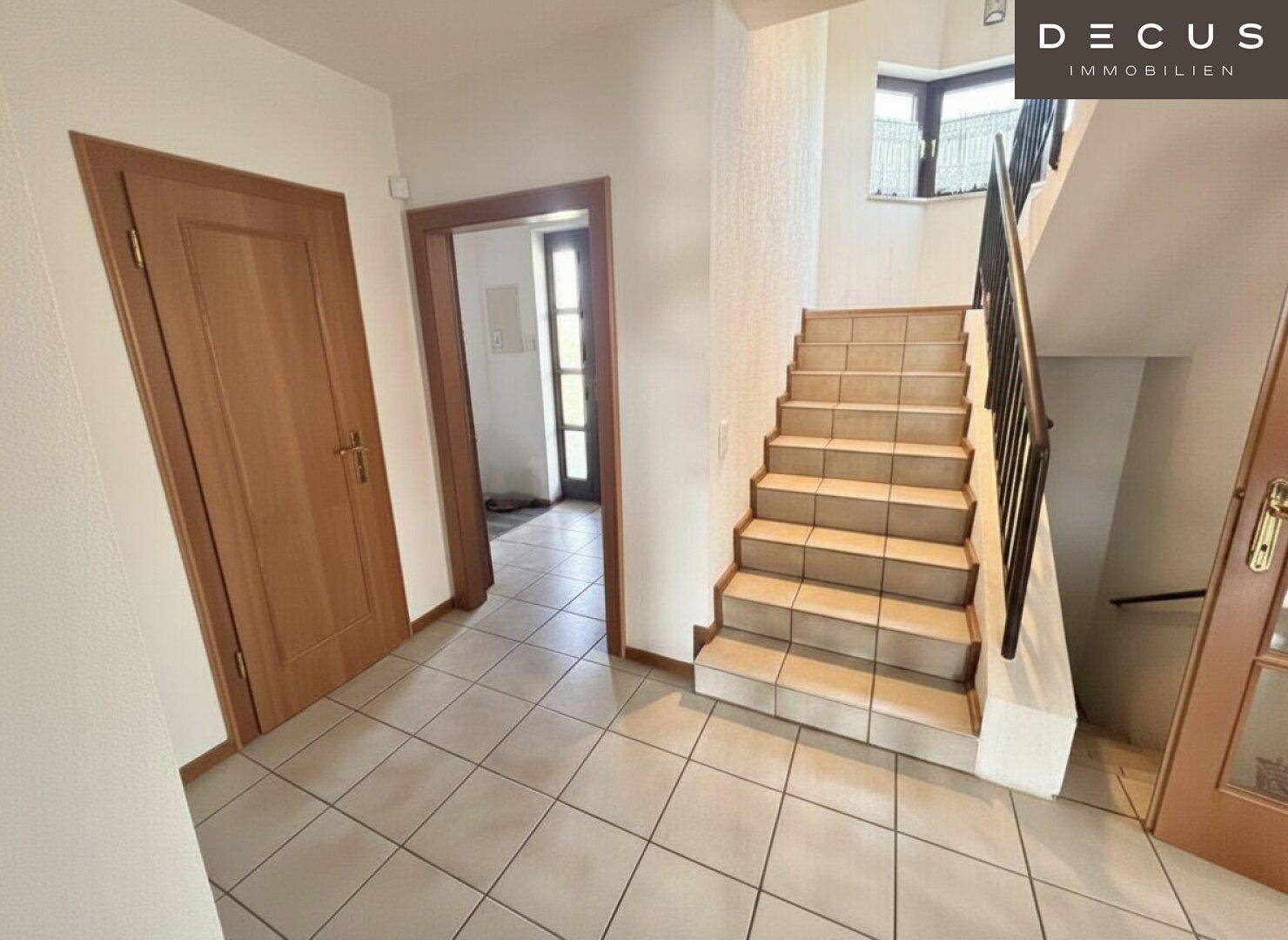 Heller Flur mit gefliestem Boden, Holztreppe und Zugang zu weiteren Räumen.