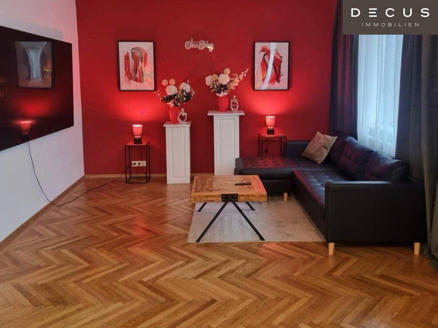 Gemütliches Wohnzimmer mit roter Akzentwand, dunklem Ecksofa und Fischgrätparkettboden.