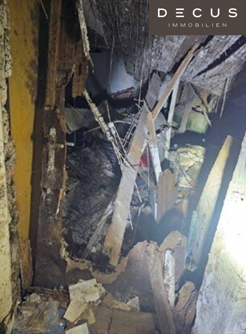 Stark zerstörter Innenraum mit freiliegenden Holzbalken und herabgefallenen Trümmern.