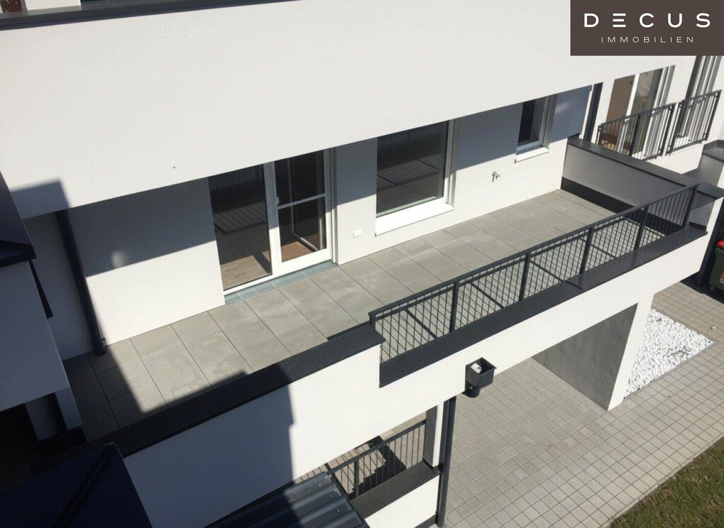 Großer Balkon mit Fliesenboden und schwarzem Geländer, von oben betrachtet.