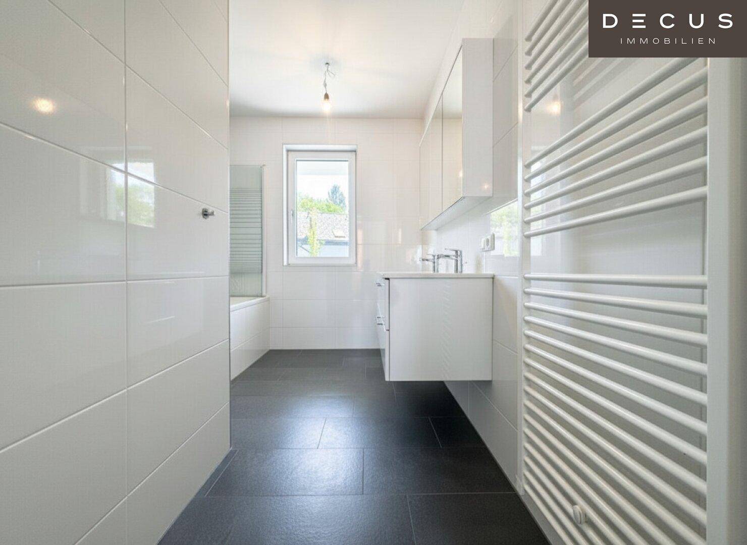 Modernes Badezimmer mit weißen Fliesen, dunklem Boden und Fenster für Tageslicht.