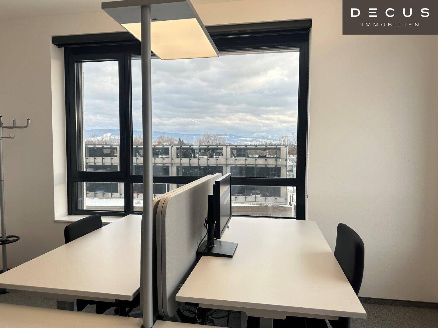 Arbeitsplatz in einem Büro mit Blick aus dem Fenster auf die umliegende Stadtlandschaft und den Himmel.