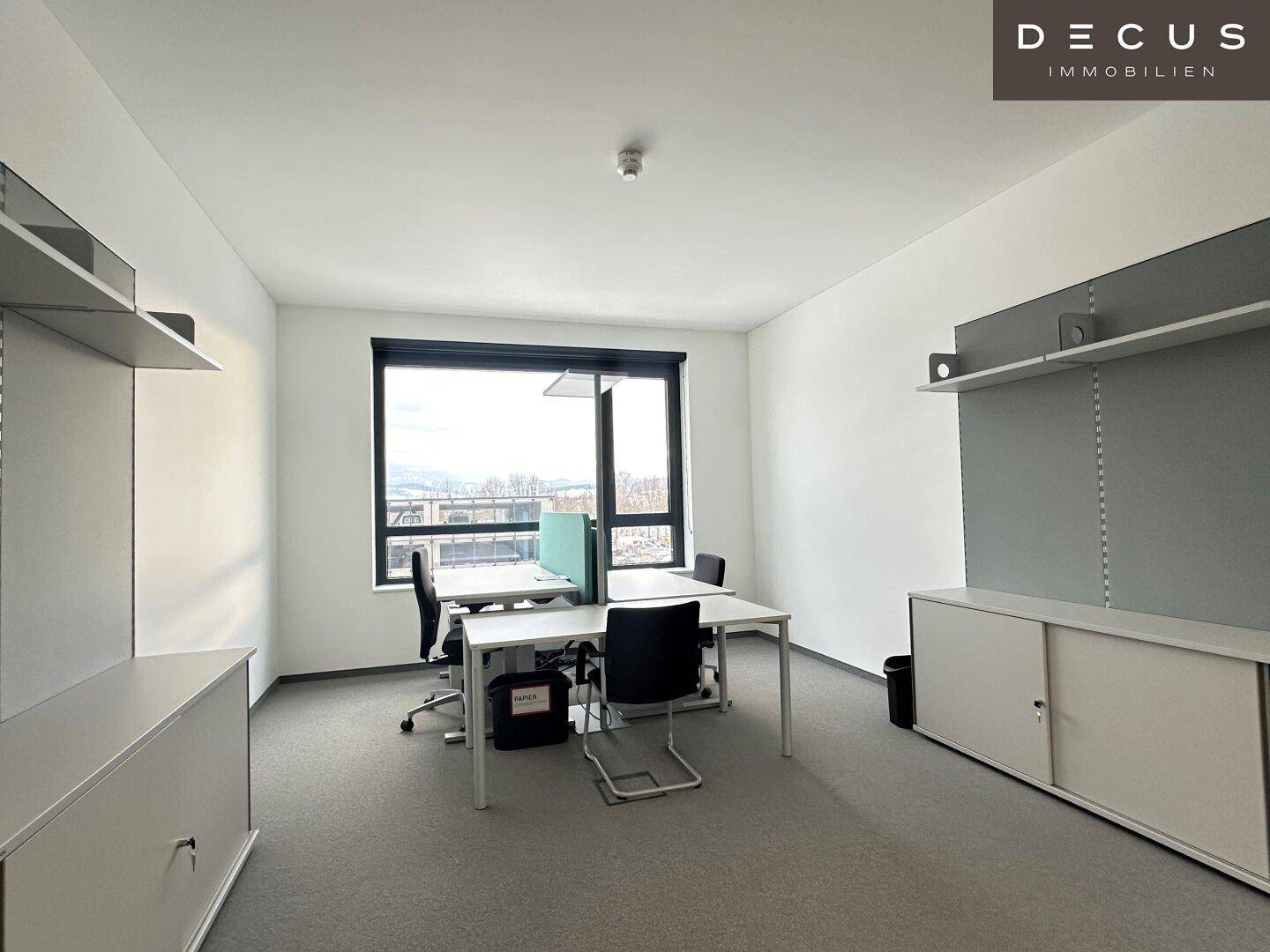 Geräumiges Büro mit mehreren Arbeitsplätzen, Stauraum und großen Fenstern, die viel Licht hereinlassen.