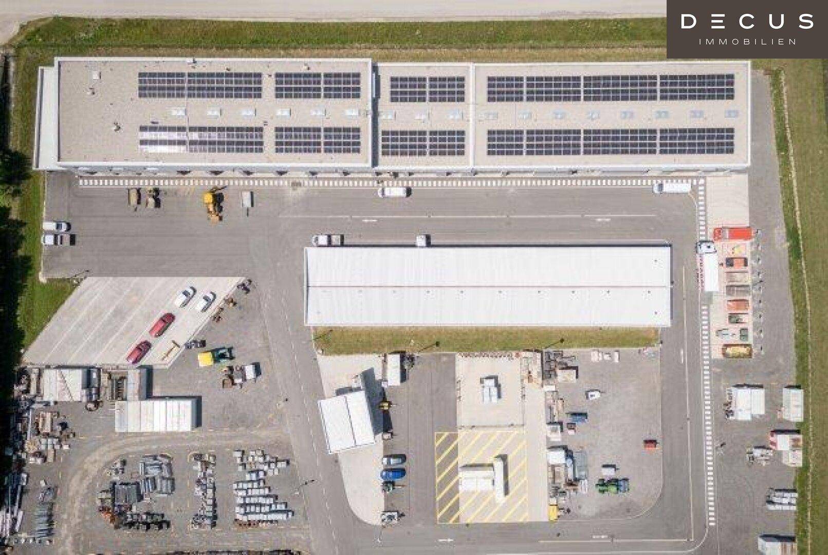 Draufsicht auf ein großes Gewerbegebäude mit umfangreichen Photovoltaikanlagen und einem weitläufigen Betriebshof.