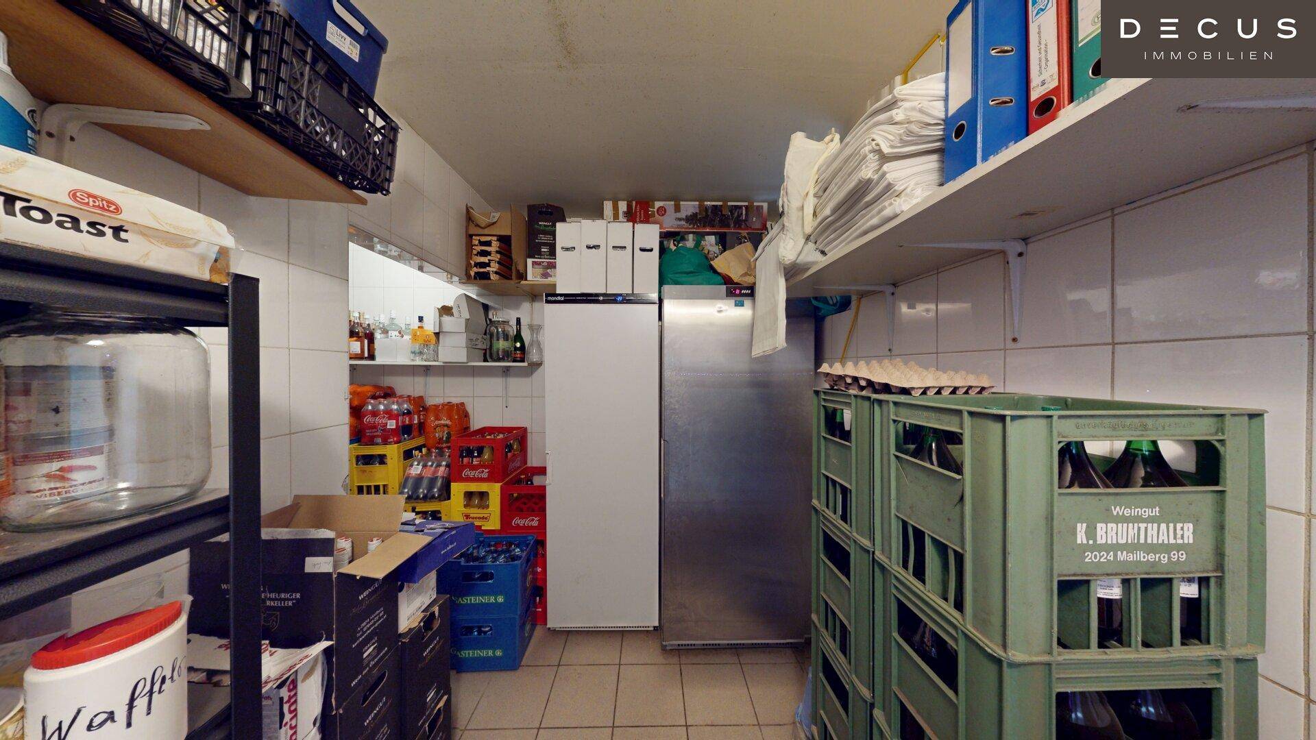Lagerraum mit Regalen voller Getränkekisten, Vorräten und einem großen Kühlschrank.