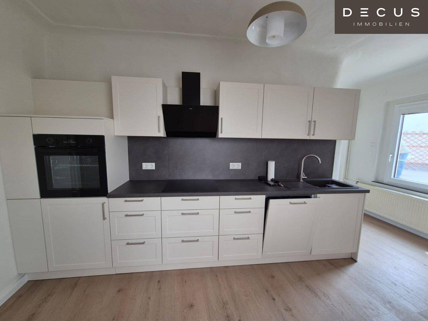 Neue Einbauküche mit weißen Fronten, integriertem Backofen und Dunstabzugshaube.