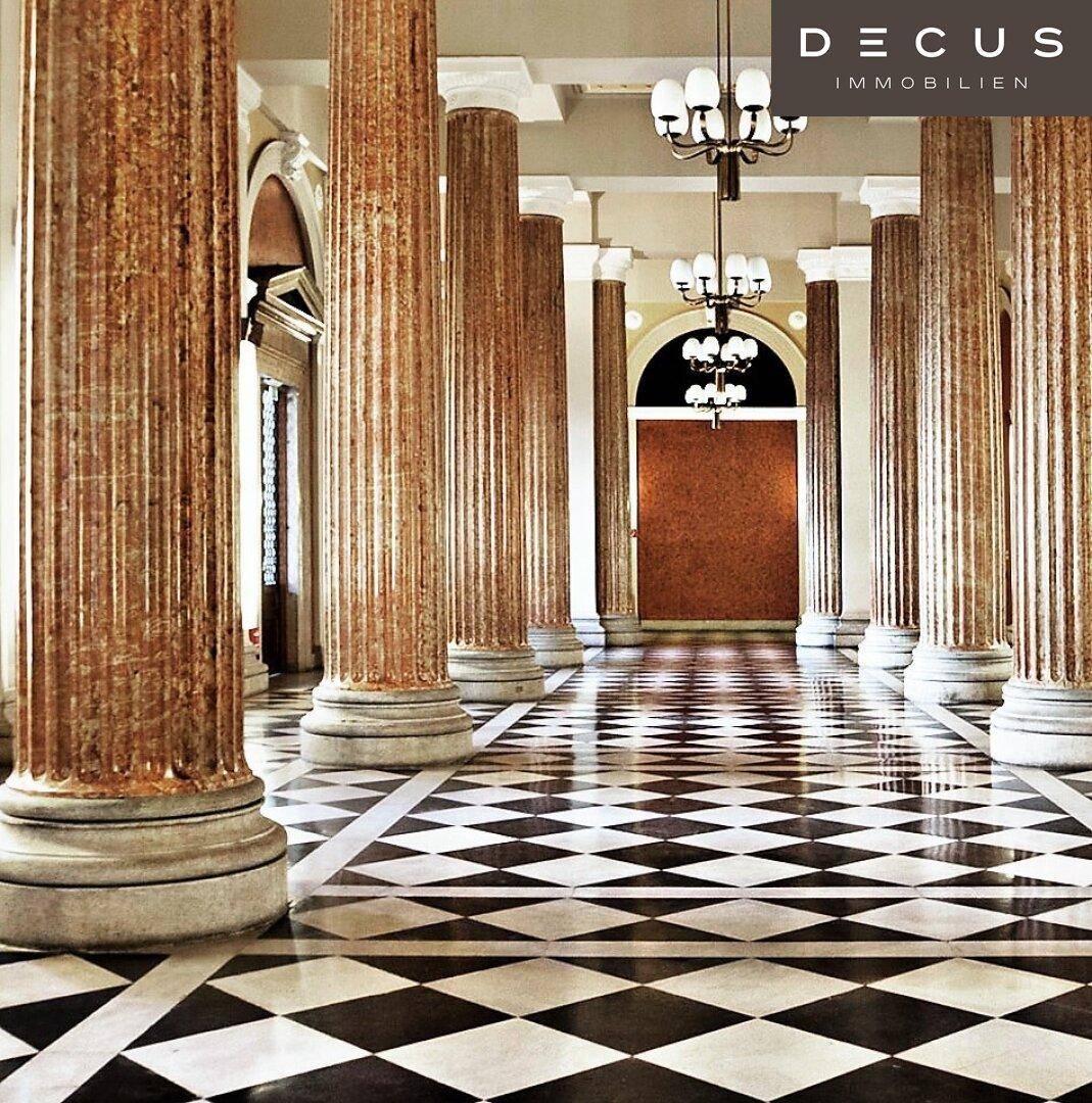 Opulenter Innenraum mit hohen Marmorsäulen, einem schwarz-weißen Schachbrettmuster-Marmorboden und eleganten Kronleuchtern.