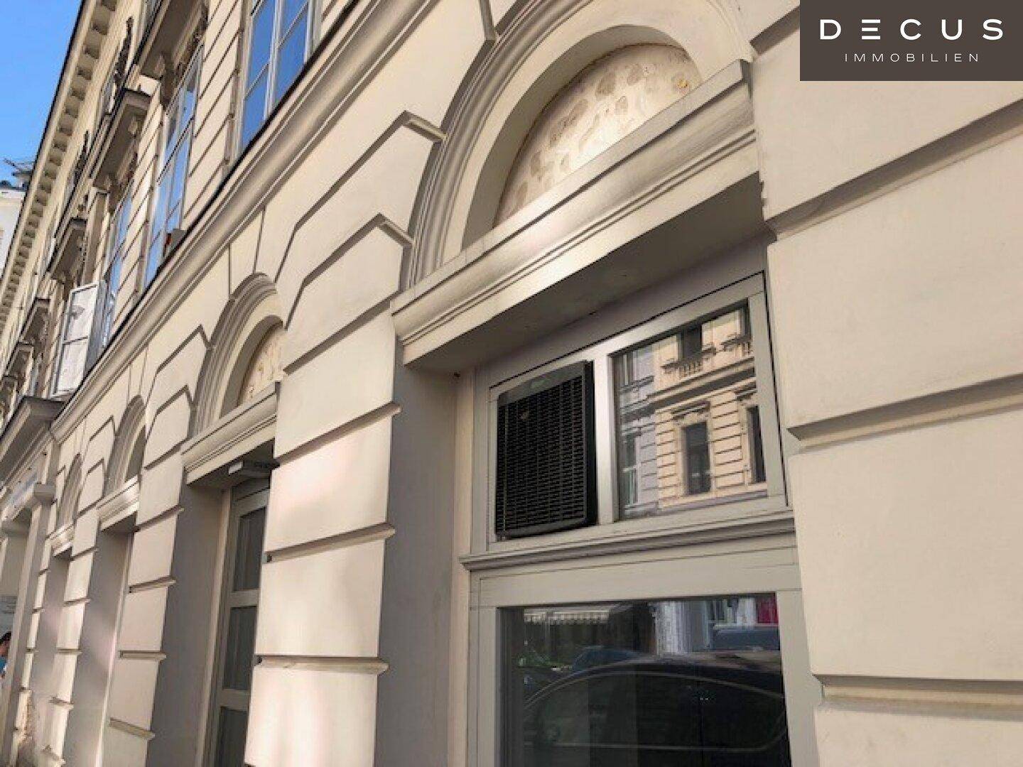 Detailansicht der historischen Fassade mit eleganten Verzierungen, großen Fenstern und einem Abluftventilator.