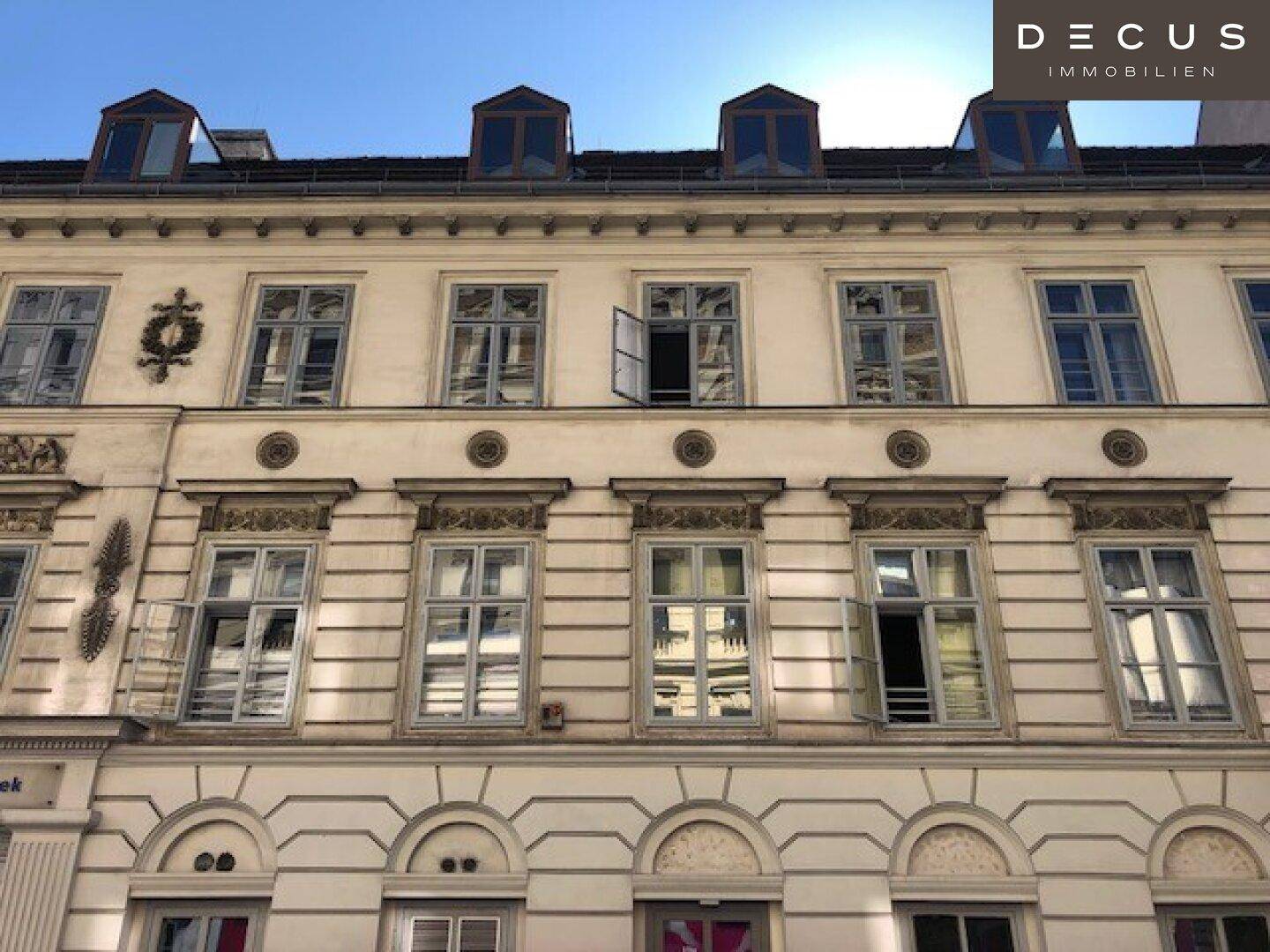 Historische Gebäudefassade mit vielen Fenstern, dekorativen Elementen und Dachgauben unter blauem Himmel.