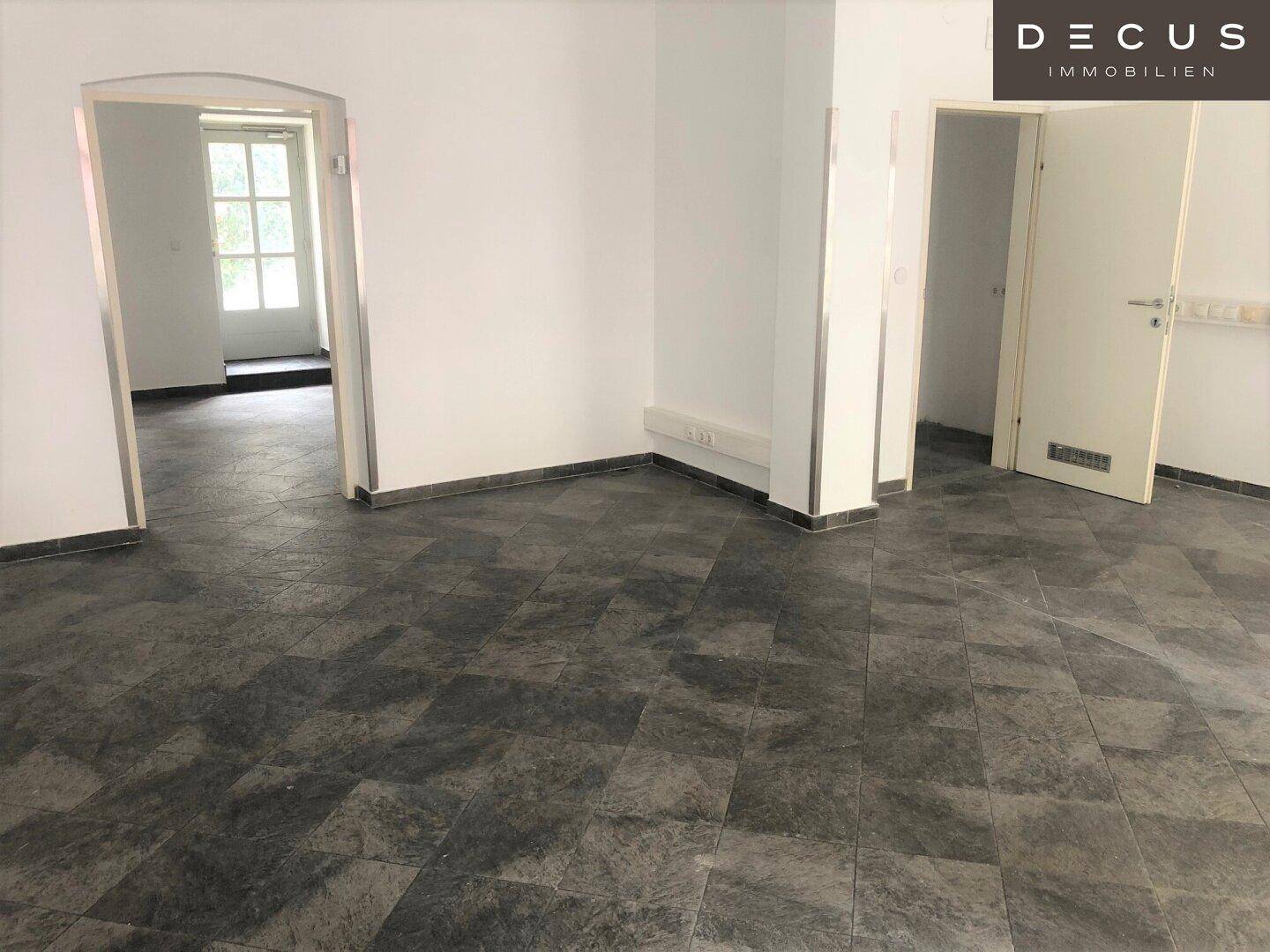 Innenansicht eines Geschäftsraums mit dunklem Fliesenboden, weiß gestrichenen Wänden und einem eleganten Bogendurchgang.