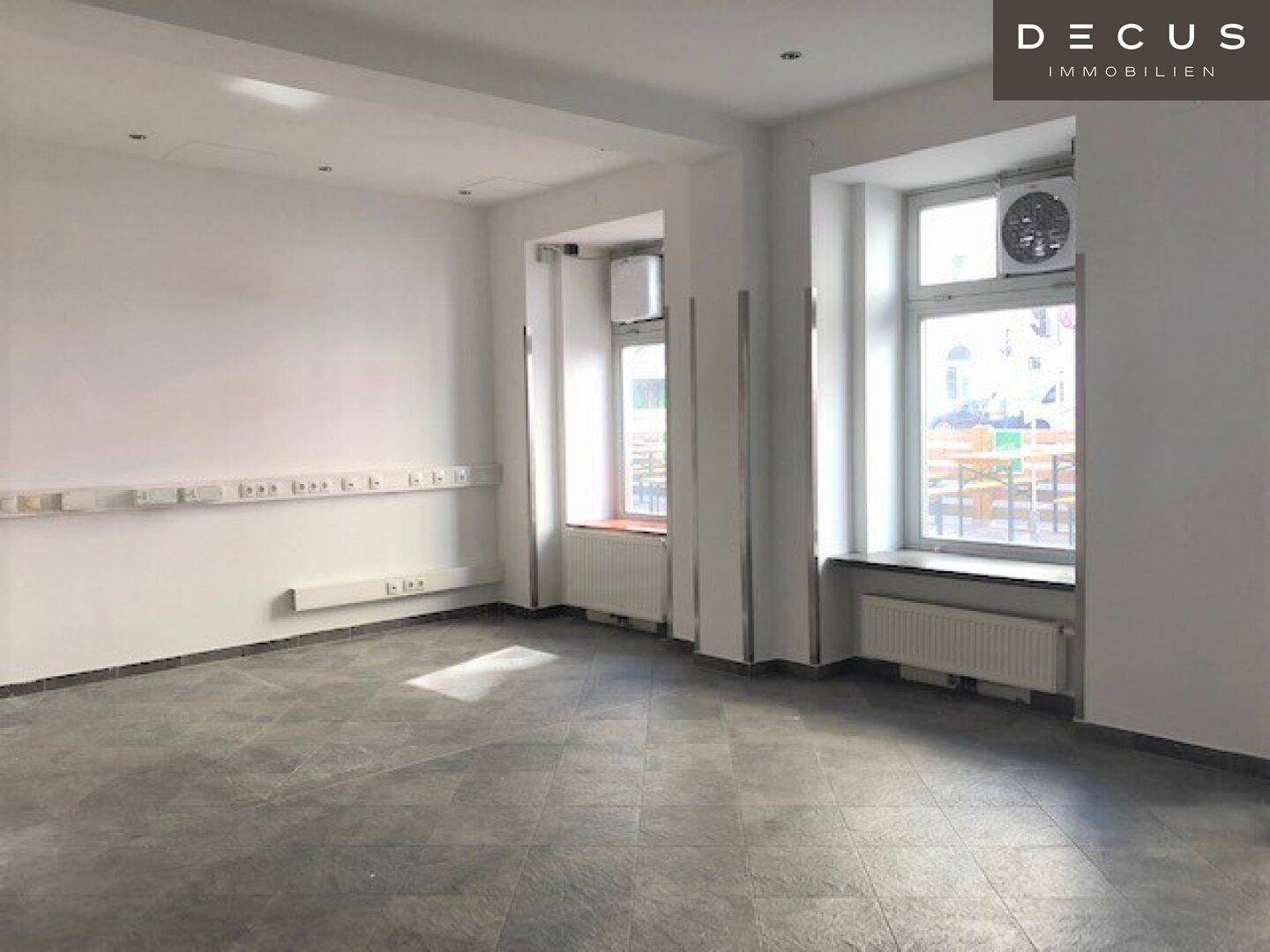 Geräumiger, heller Geschäftsraum mit vielen Steckdosen entlang der Wand und großen Fenstern, die viel Licht hereinlassen.