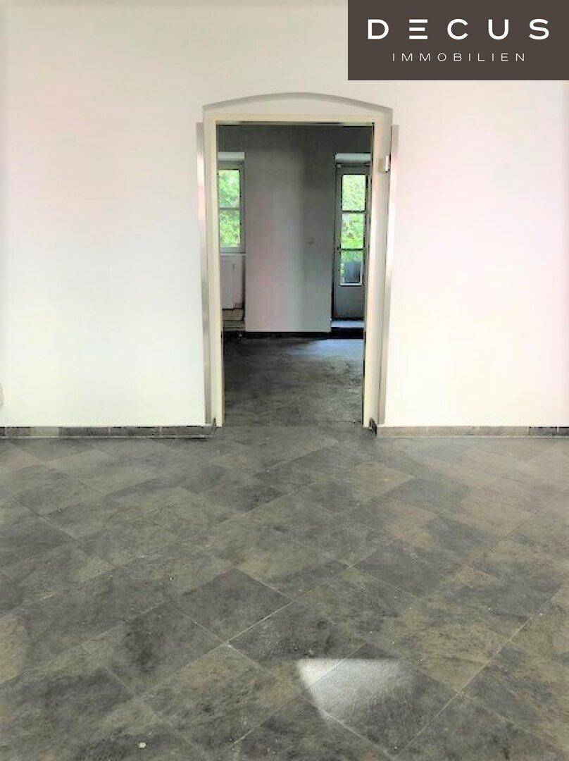 Blick durch einen eleganten Bogendurchgang in einen weiteren Raum mit Fenstern und viel Tageslicht.