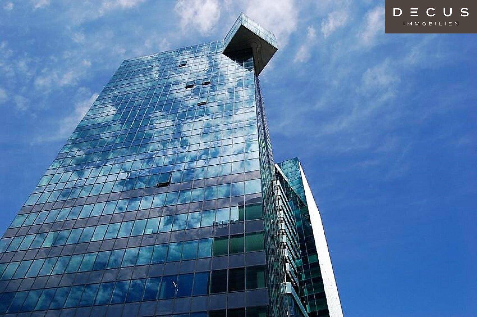 Beeindruckendes modernes Hochhaus mit spiegelnder Glasfassade, das den blauen Himmel und Wolken reflektiert.