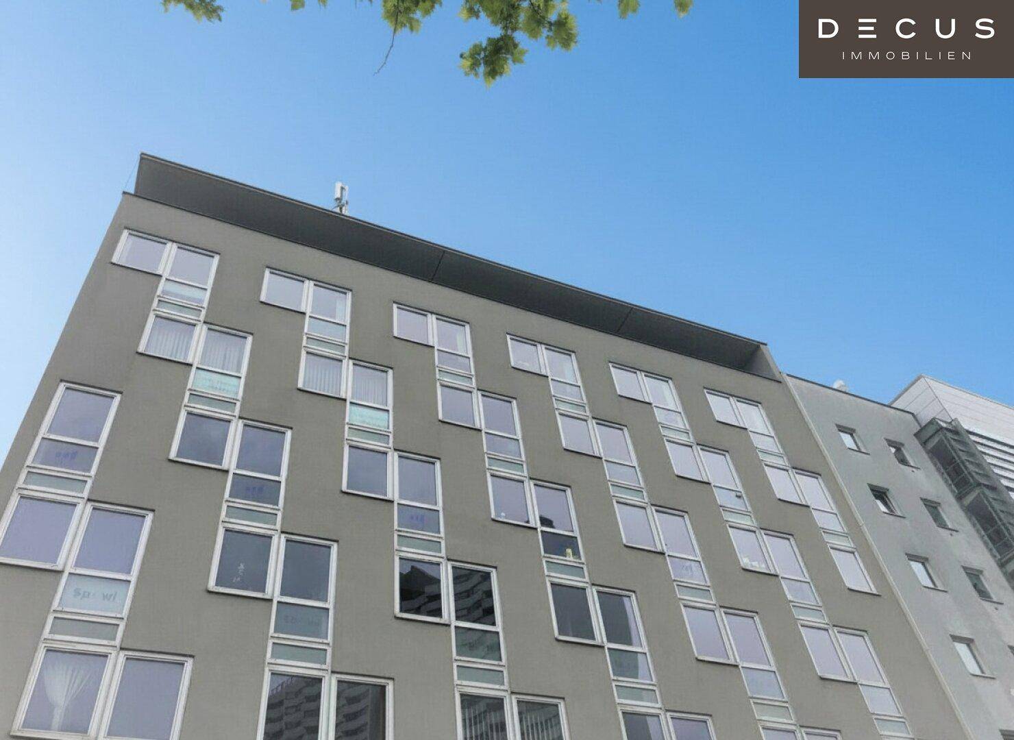 Ansicht eines modernen Gebäudes mit vielen Fenstern und einer klaren, geradlinigen Architektur unter blauem Himmel.