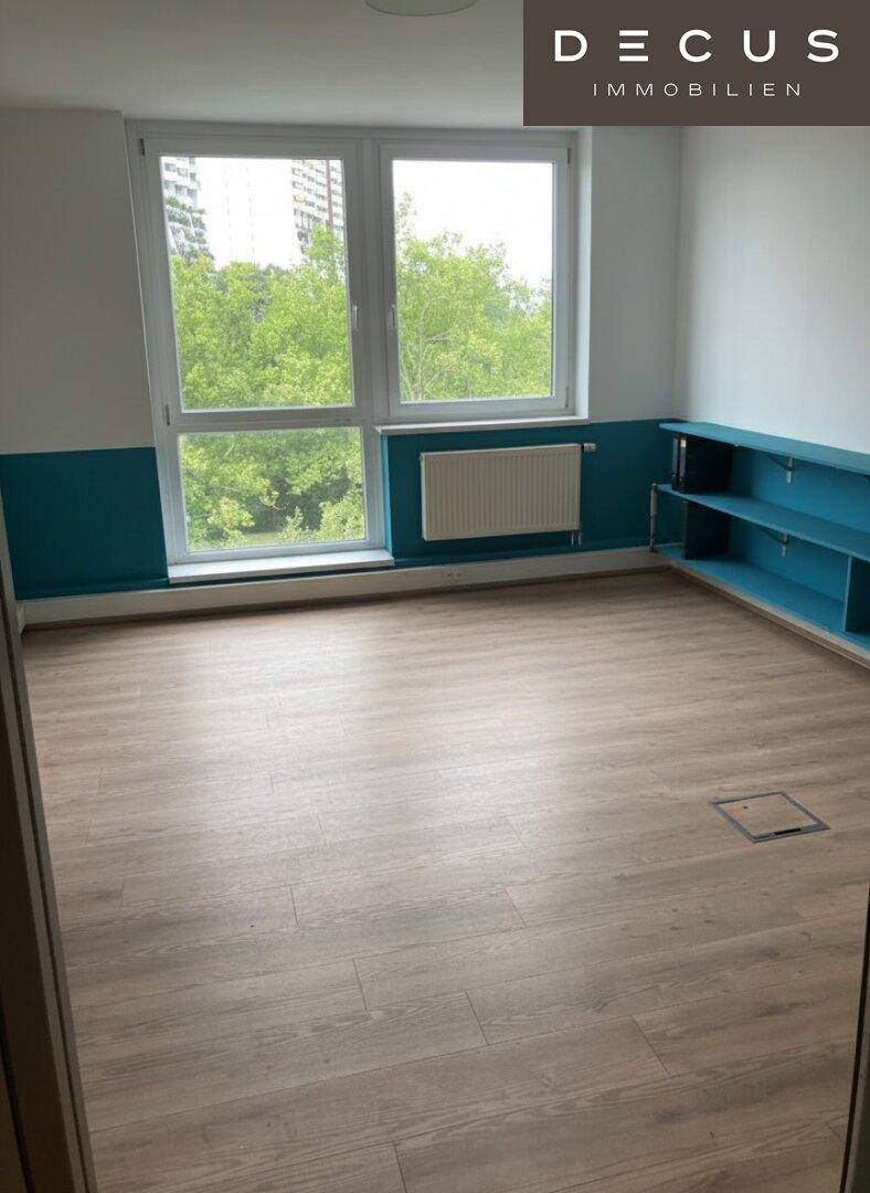 Geräumiger Raum mit Laminatboden, großen Fenstern und einer blauen Wandgestaltung mit integrierten Regalen.