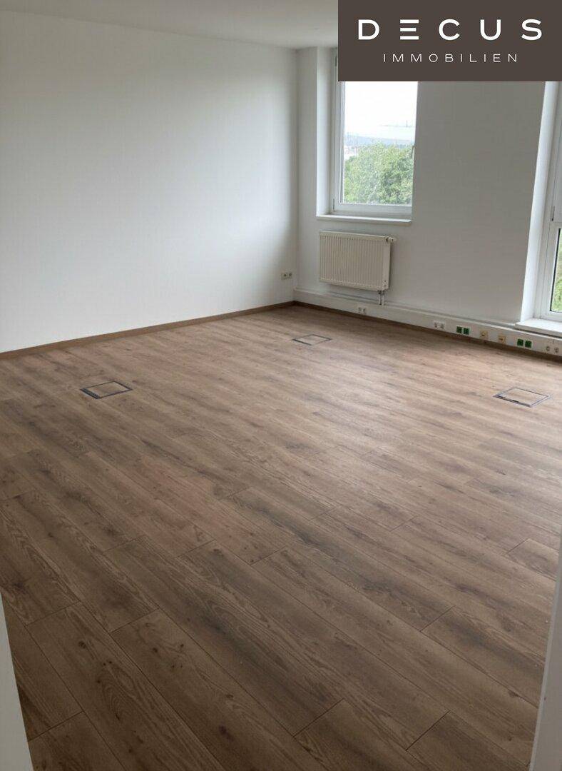 Leerer Raum mit warmem Laminatboden und mehreren Fenstern, die für ausreichend Helligkeit sorgen.