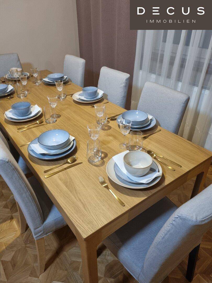 Heller Essbereich mit Holztisch und Stühlen, elegant gedeckt für mehrere Personen.