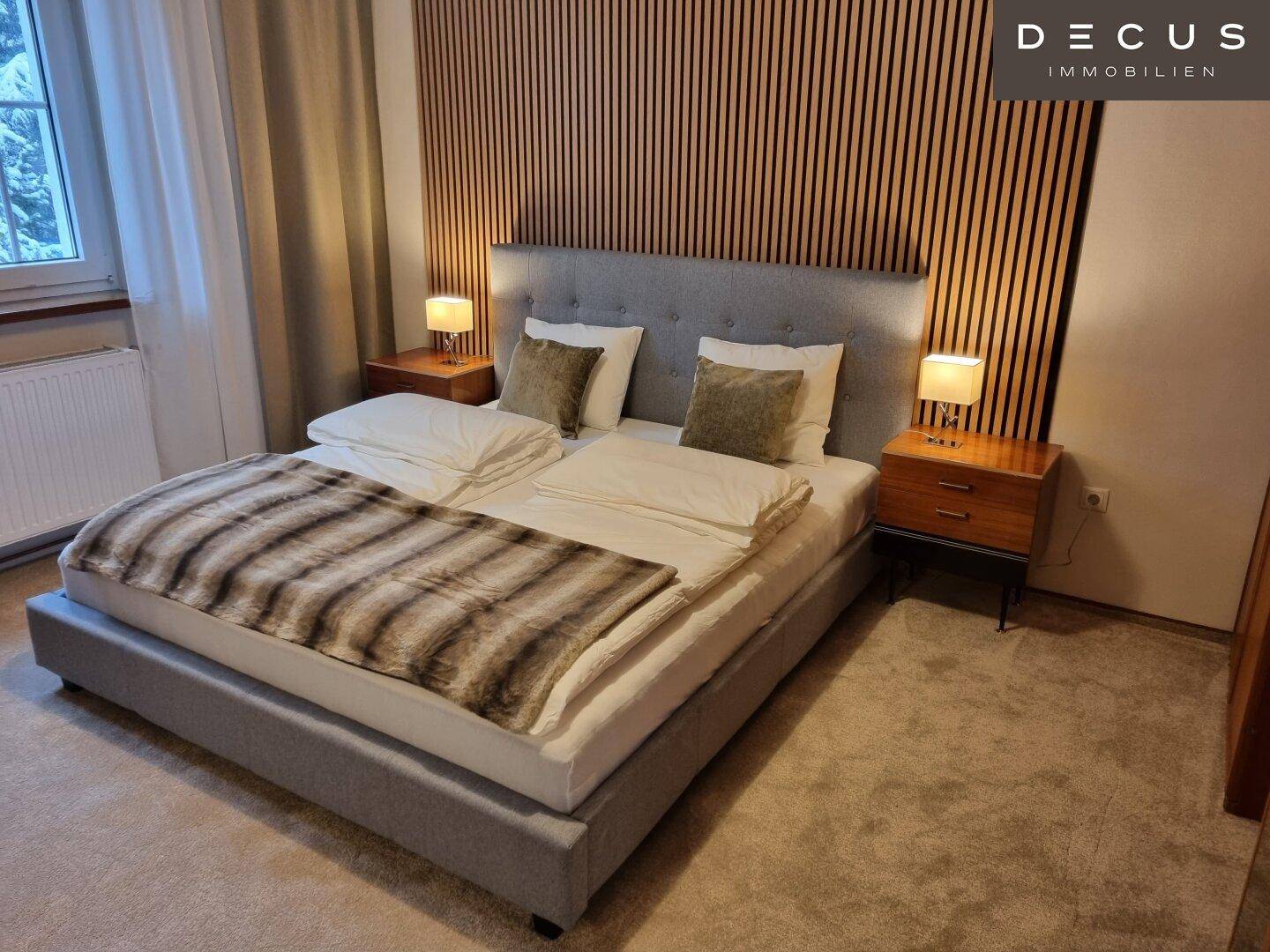 Schlafzimmer mit Doppelbett, Holzwandverkleidung und Teppichboden in warmen Farben.
