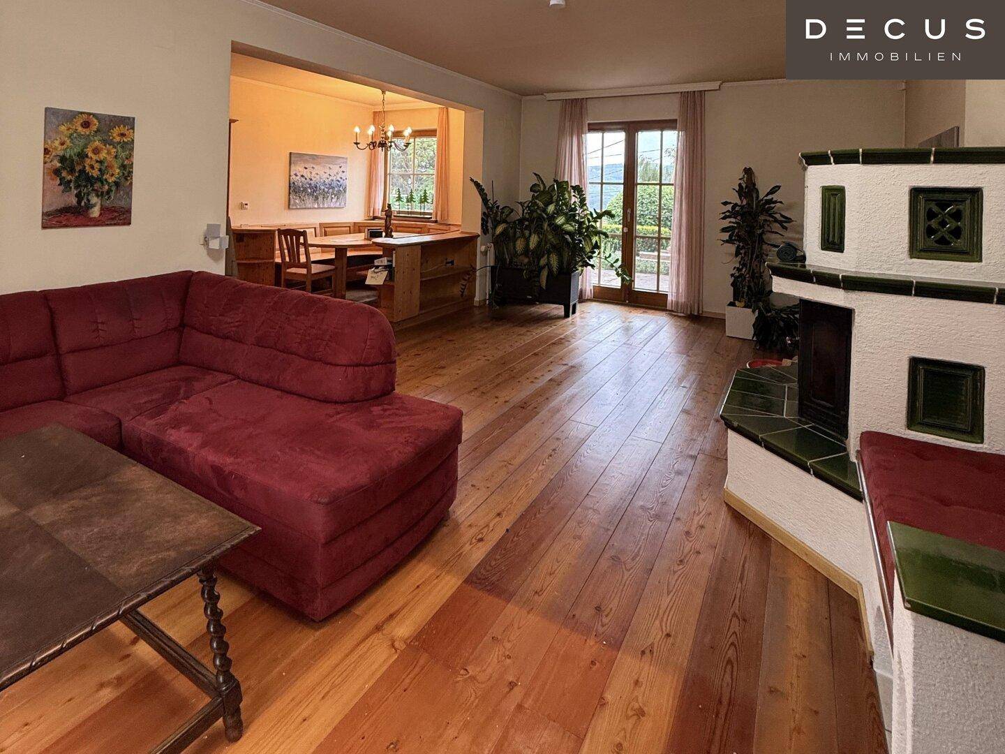 Gemütliches Wohnzimmer mit Holzdielenboden, Kachelofen und Zugang zum Garten.