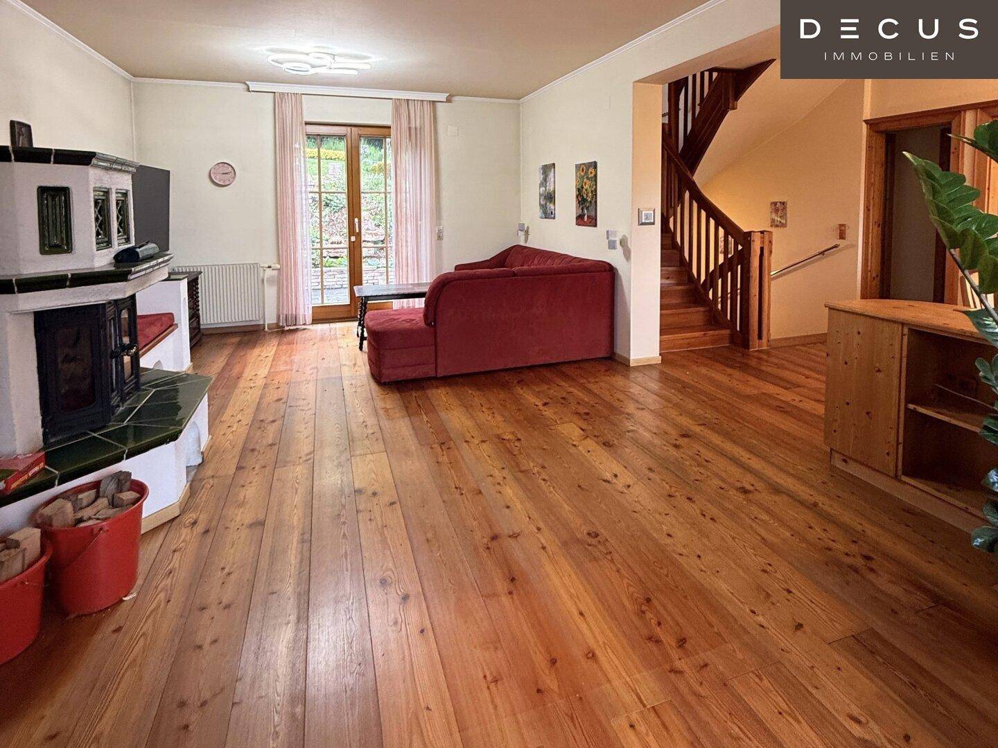 Geräumiges Wohnzimmer mit Kachelofen, Holzdielen und Blick auf die Holztreppe.