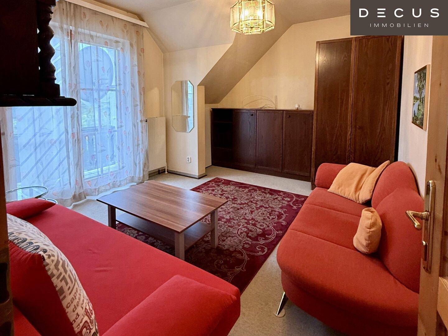 Helles Schlafzimmer im Dachgeschoss mit rotem Sofa, Teppich und Dachschräge.