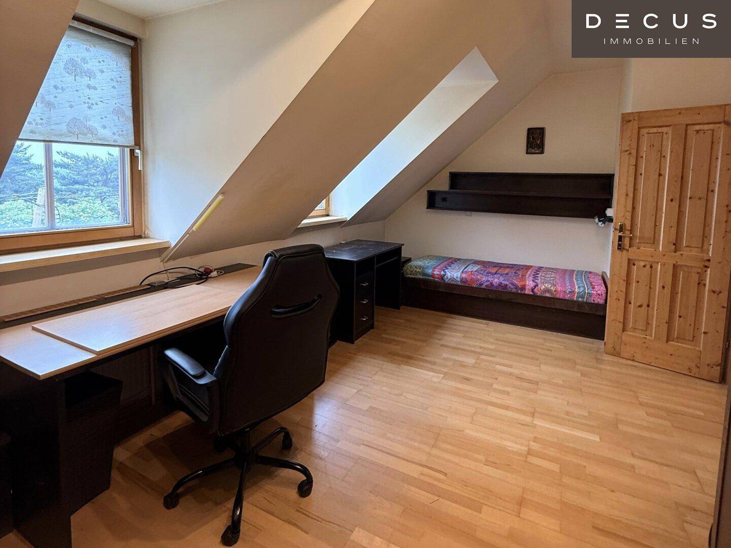 Schlafzimmer im Dachgeschoss mit Holzboden, Schreibtisch und Einzelbett.