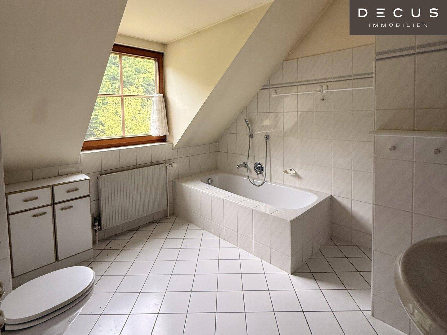 Badezimmer im Dachgeschoss mit Badewanne, WC und weißen Fliesen.