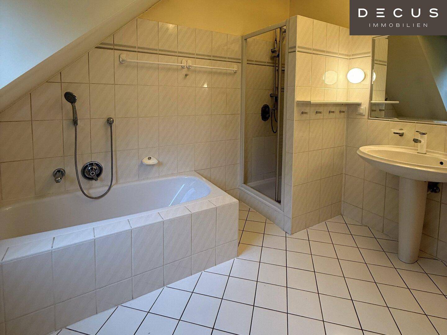 Badezimmer im Dachgeschoss mit Badewanne, Dusche, Waschbecken und weißen Fliesen.