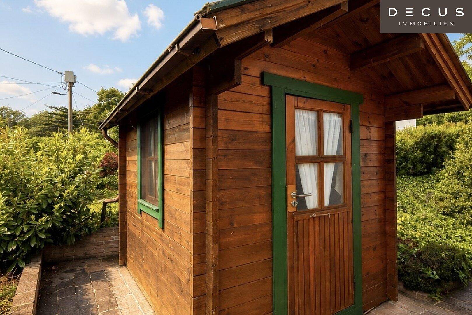 Rustikales Gartenhaus aus Holz mit grünen Akzenten, umgeben von üppigem Grün im Garten.