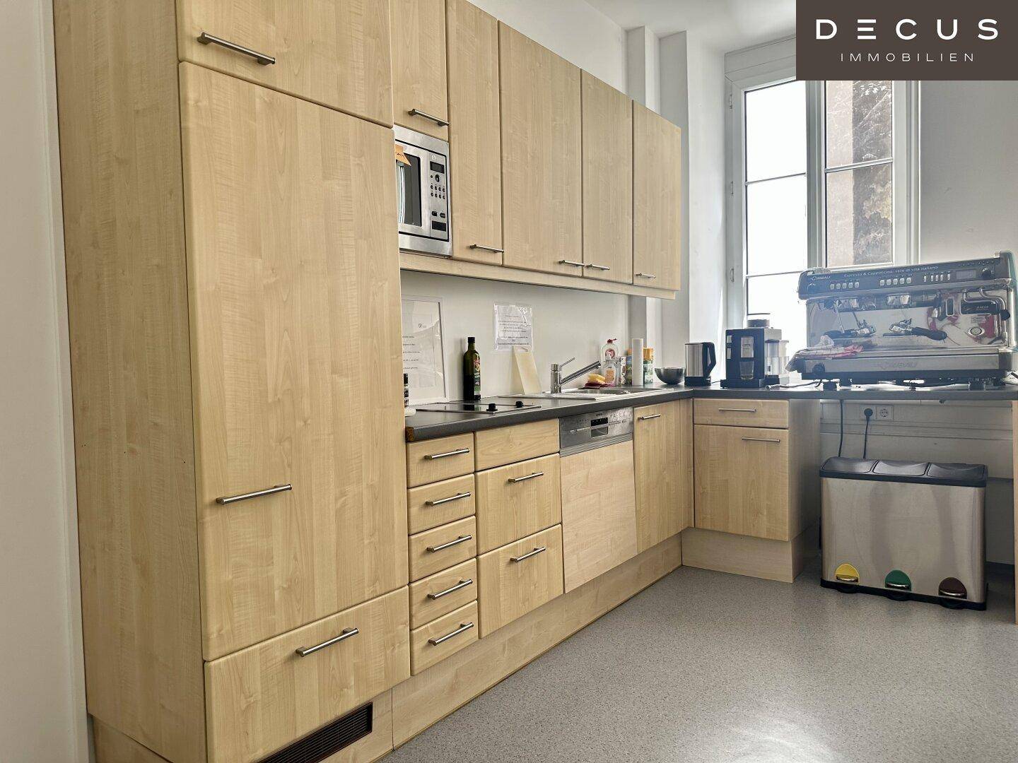 Funktionale Teeküche mit hellen Holzschränken, Mikrowelle, Geschirrspüler und Kaffeemaschine.