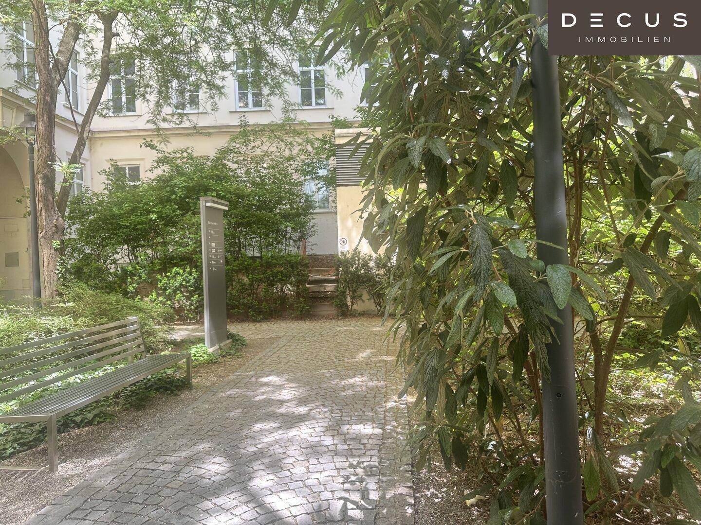 Ruhiger Innenhof mit Bäumen, Bänken und einem gepflasterten Weg, ideal zum Entspannen.