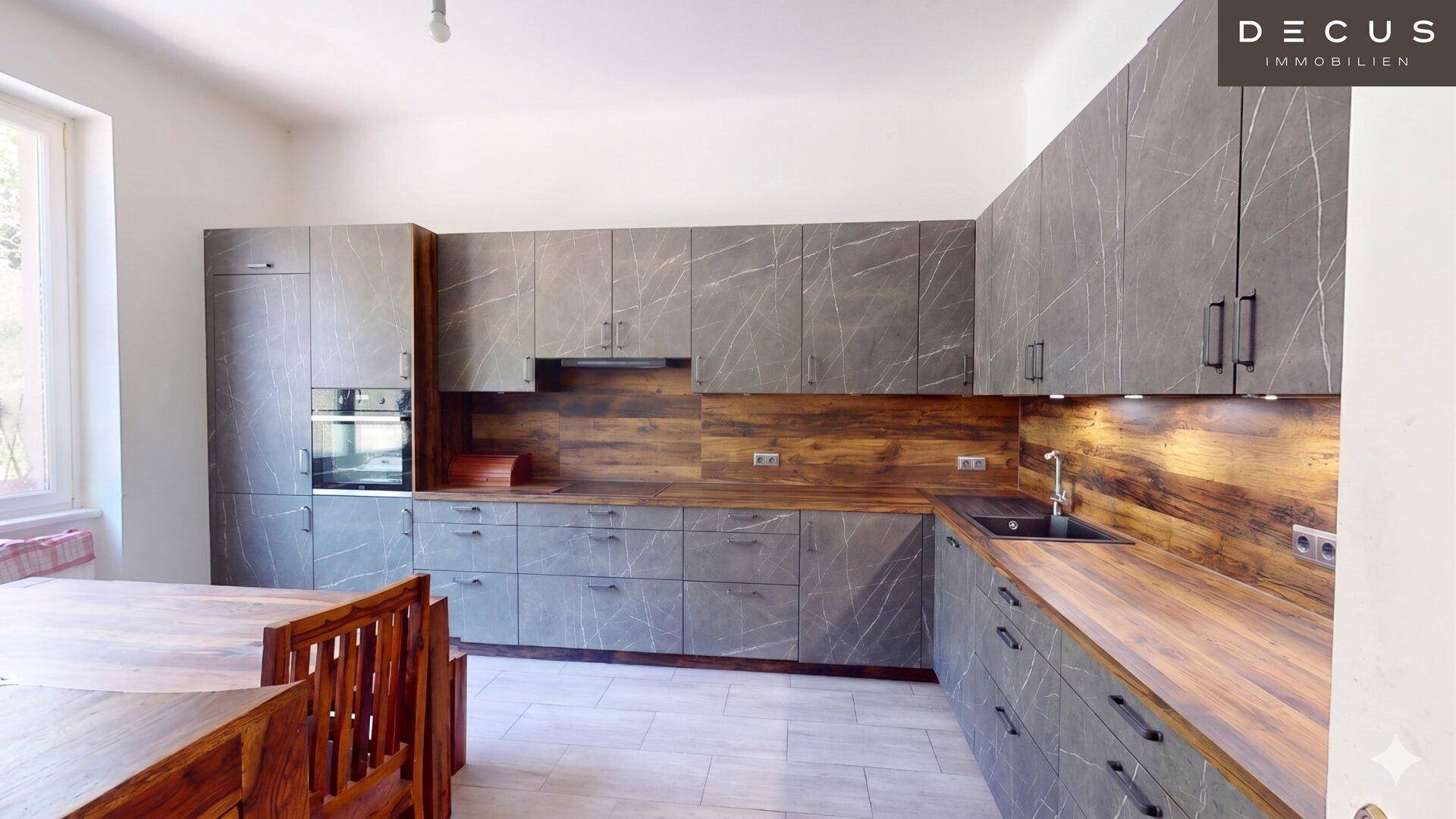 Moderne Küche mit grauen Fronten in Marmoroptik, Holzarbeitsplatten und Essbereich.