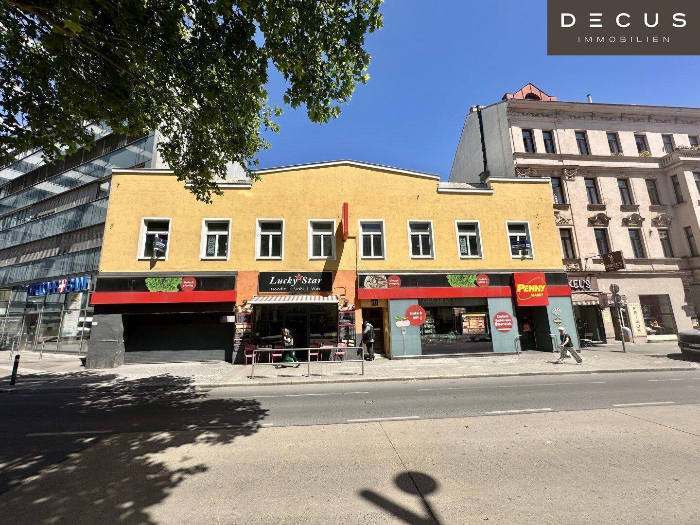 Gelbes Geschäftsgebäude an einer belebten Straße mit Geschäften im Erdgeschoss und Wohnungen darüber.