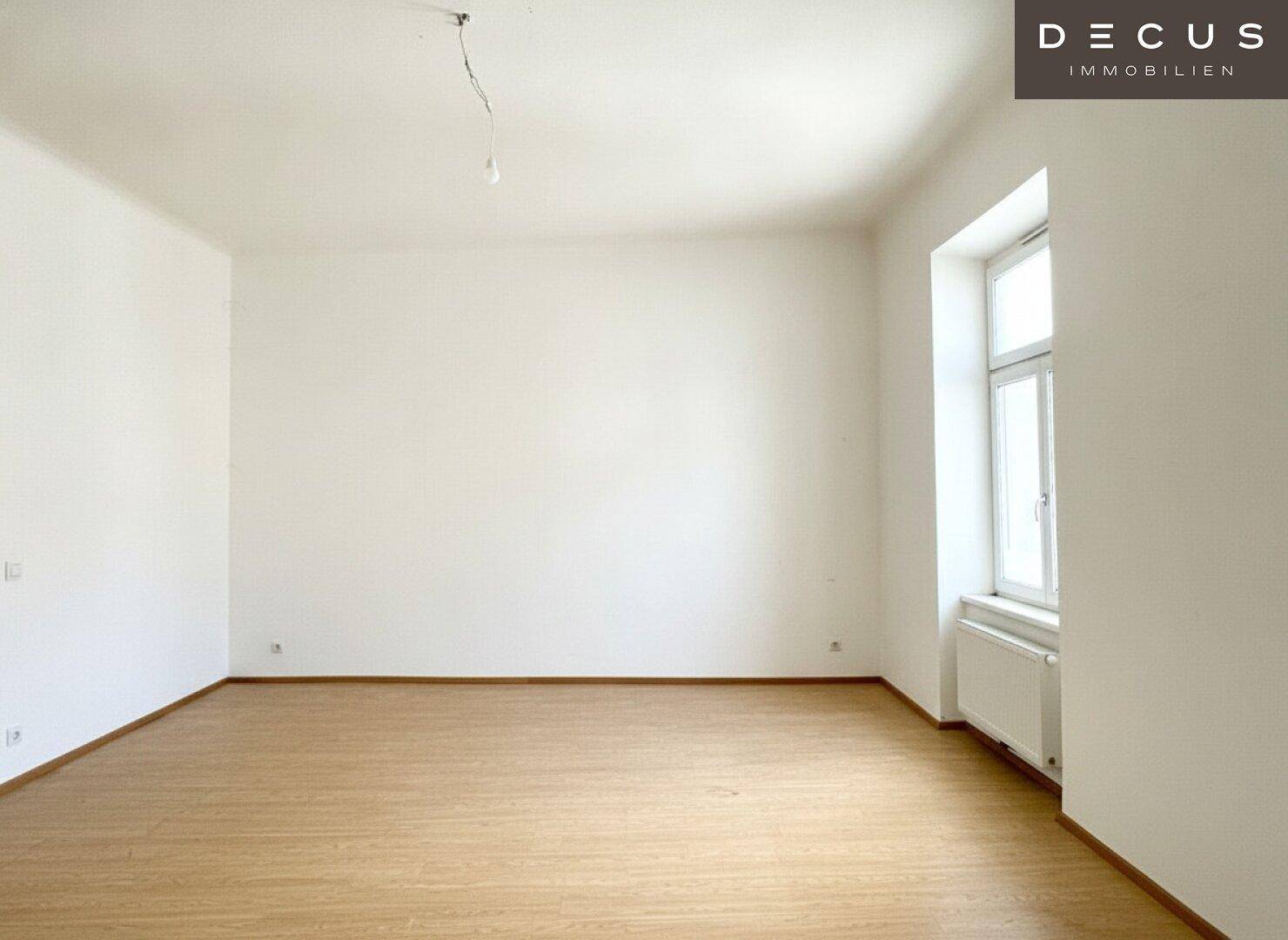 Geräumiger, leerer Raum mit hellen Holzböden und einem Fenster, das viel Tageslicht hereinlässt.