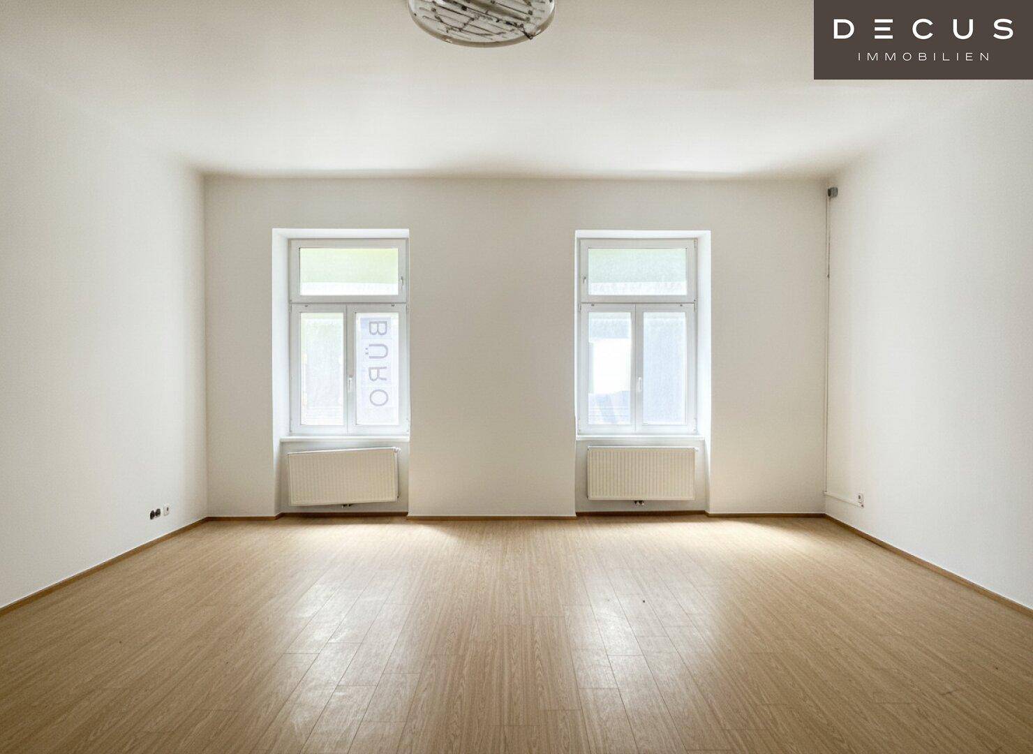 Großer, heller Raum mit zwei Fenstern, die viel Tageslicht bieten, und einem Holzboden.