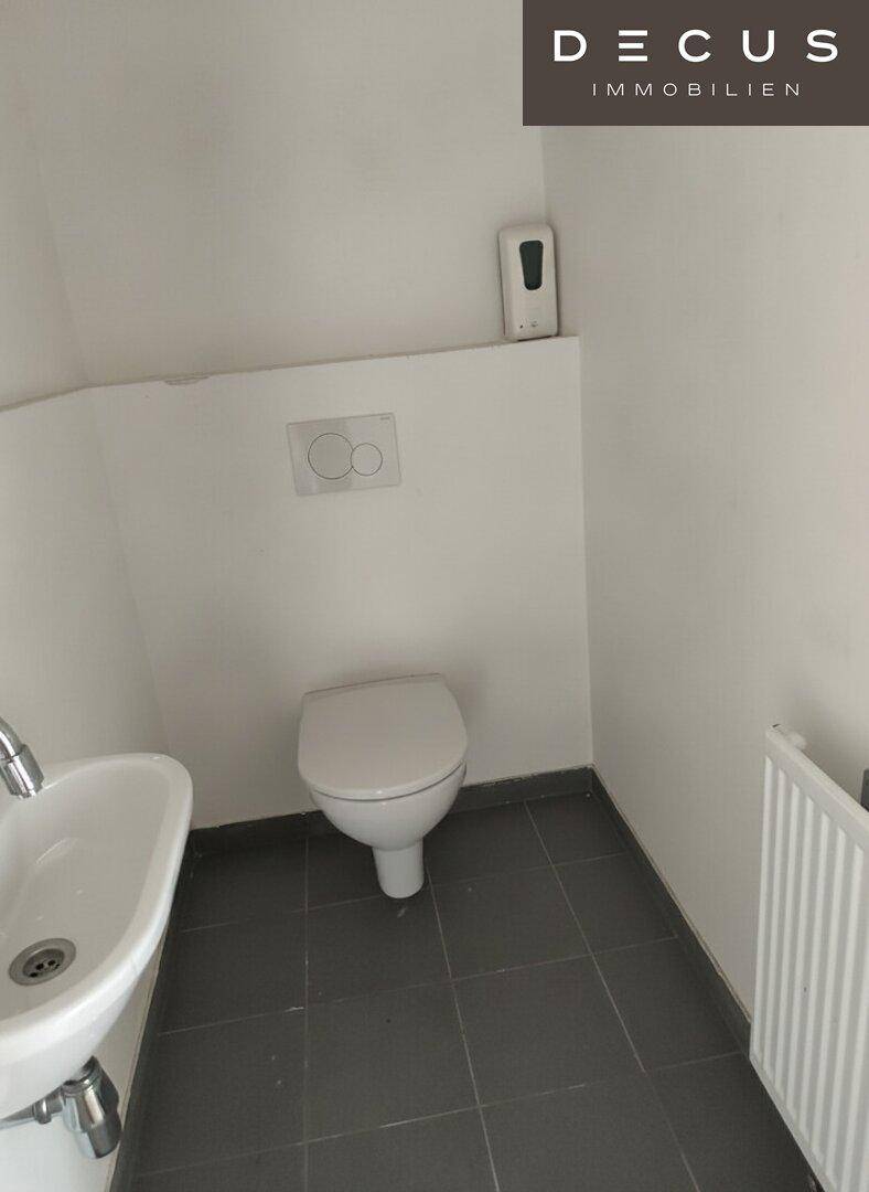 Modernes Gäste-WC mit Wand-WC, kleinem Waschbecken und dunklen Fliesen auf dem Boden.