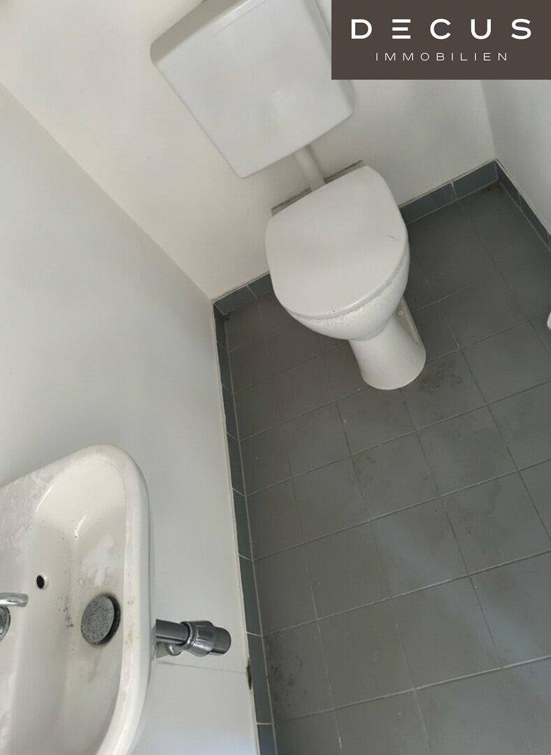 Kleines Badezimmer mit WC und Waschbecken, ausgestattet mit grauen Bodenfliesen.