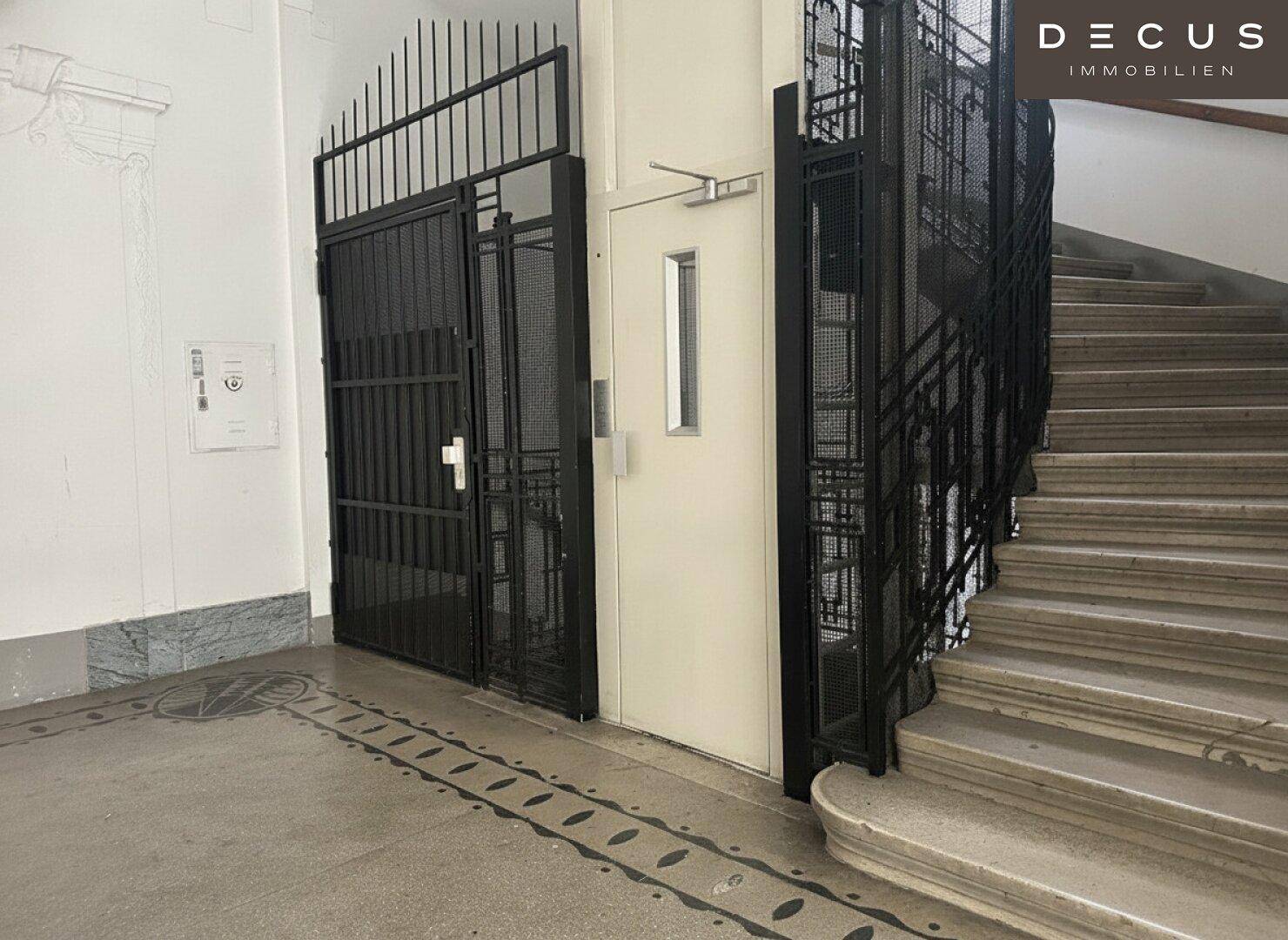 Eingangsbereich mit modernem Aufzug und Treppenhaus in einem Altbau.