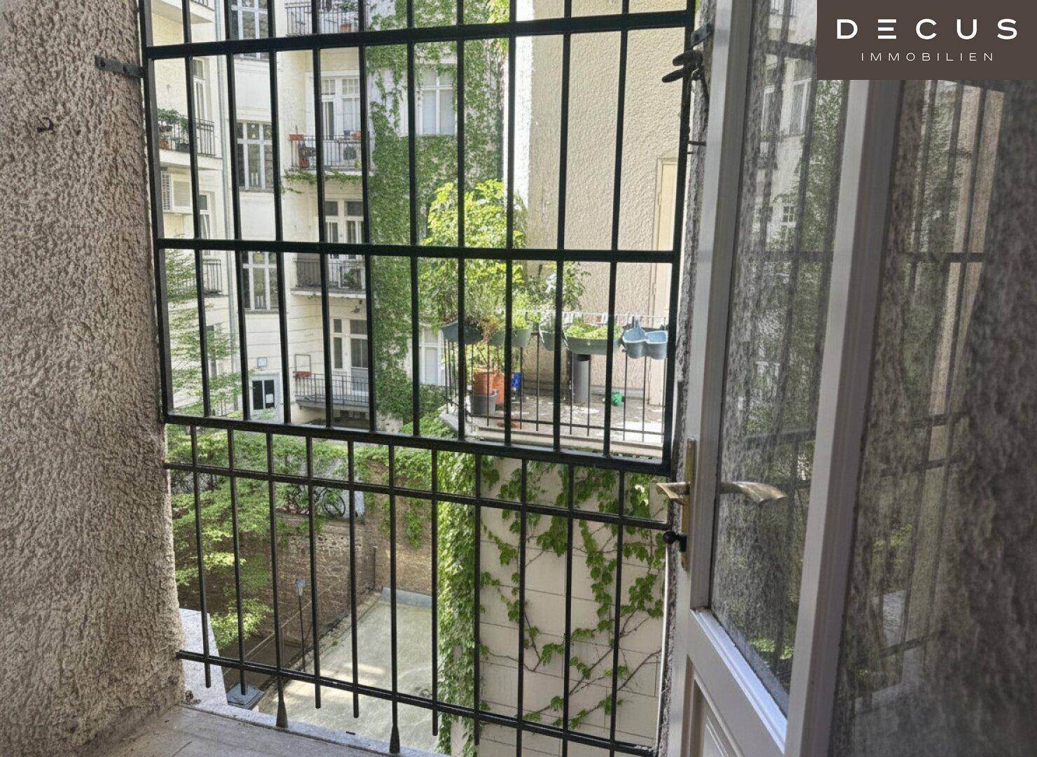 Kleiner Balkon mit Gitter und Blick auf einen begrünten Innenhof.