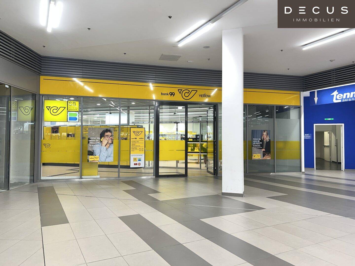 Helle Bankfiliale mit gelber Beschilderung und großen Schaufenstern in einem belebten Einkaufszentrum.